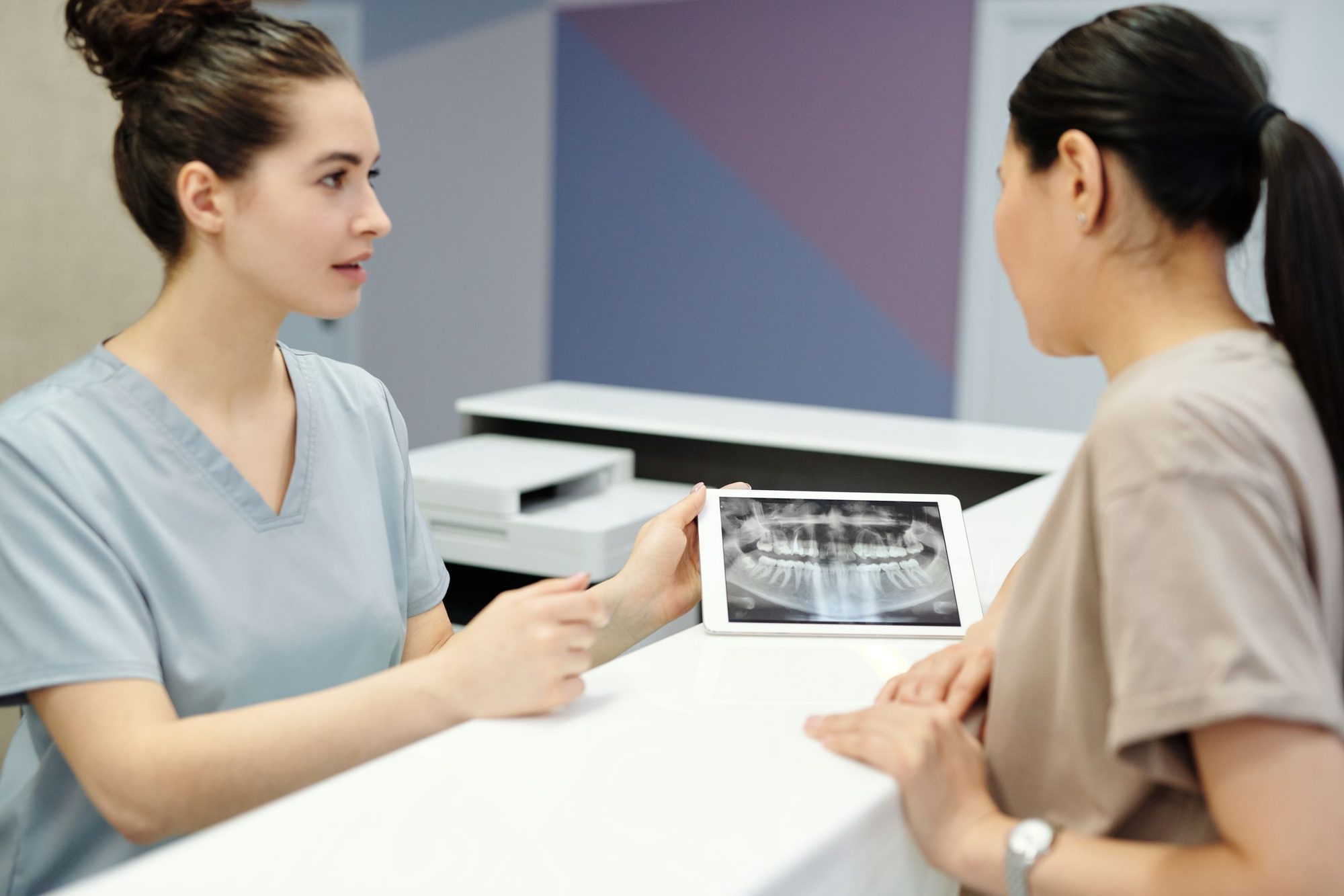 Asistentă medicală care îi arată unei paciente o radiografie panoramică pe o tabletă